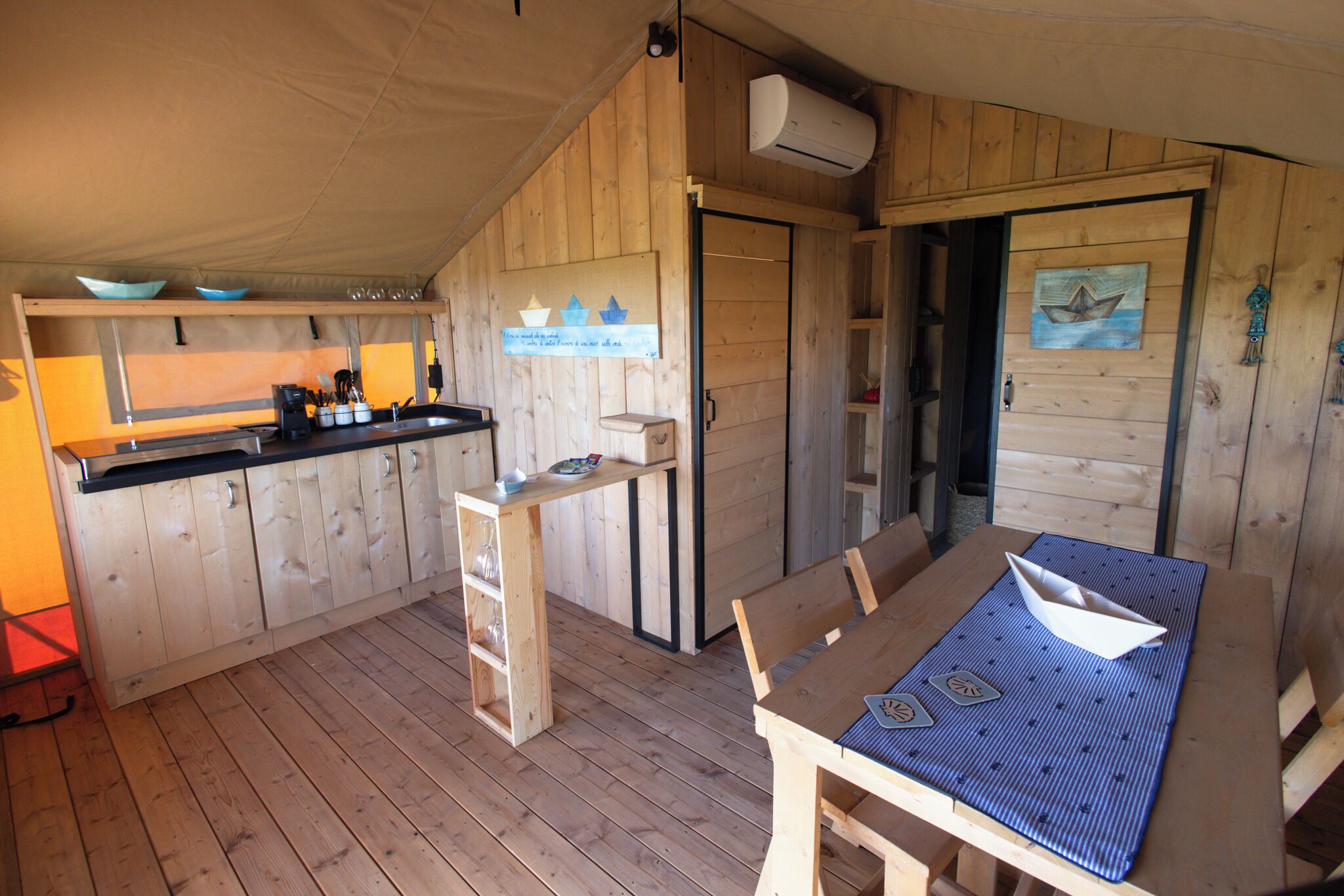 Une cabane en bois comprenant un coin cuisine, une table à manger avec un set de table et une petite étagère avec des ustensiles de cuisine.
