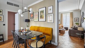 A dining area with a glass table, black chairs, a yellow sofa, and framed pictures on the wall. - Magnificent new Apartment Notre Dame de Paris (Paris)