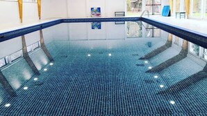 Una piscina interior con suelo de baldosas azules, vigas de madera en el techo y un banco cerca del borde de la piscina.