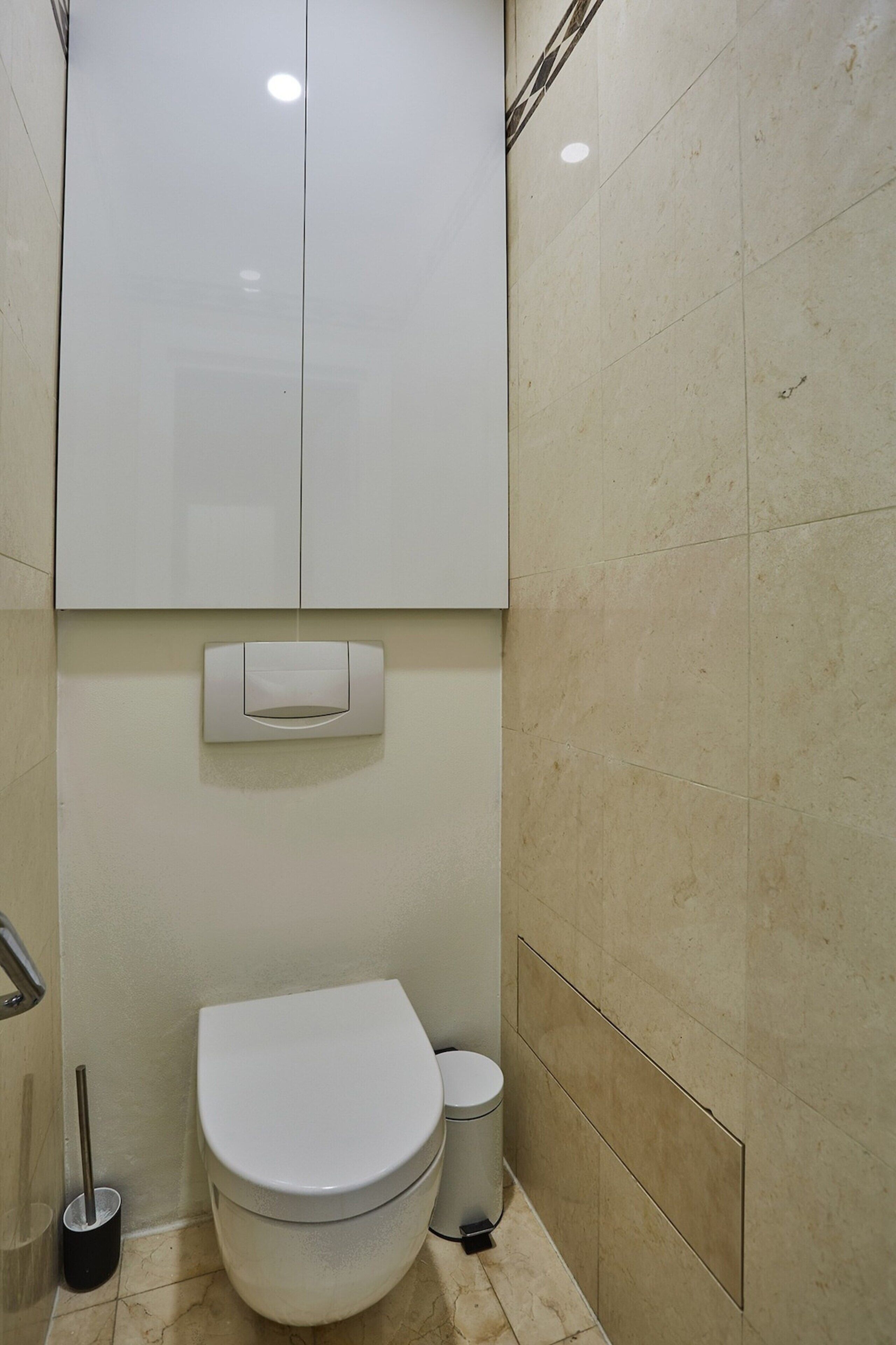 A bathroom with a toilet, a trash bin, and a hand dryer mounted on the wall.