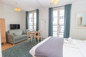 A hotel room with a bed, a sofa, a TV, a dining table, and a window with curtains. - Superb and New Studio in the Center of Paris (Paris)