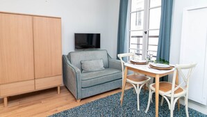 A compact living space with a sofa, a TV, a dining table with chairs, and a wardrobe.