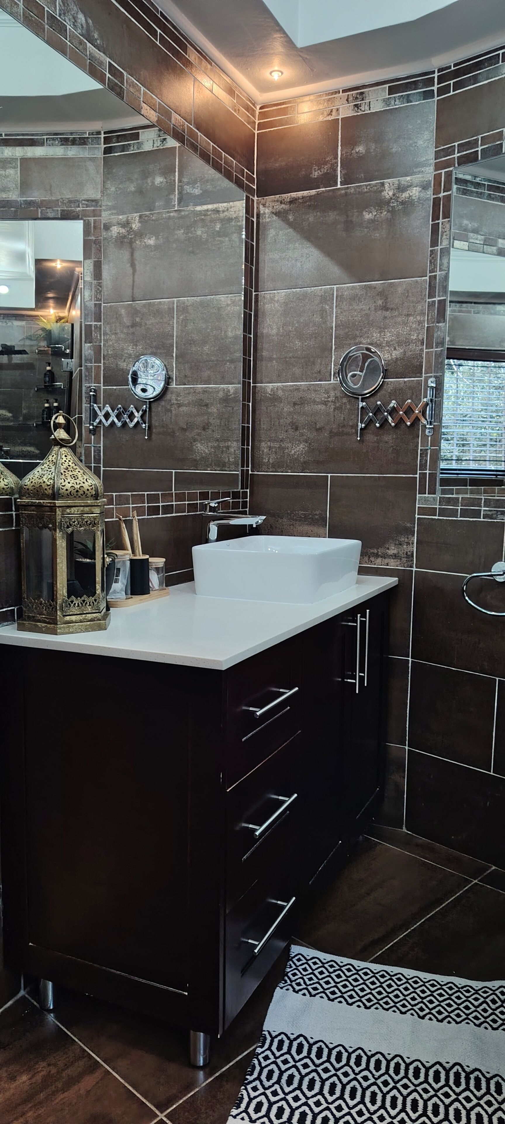 A modern bathroom with a large dark-toned sink, a mirror, and a decorative wall tile pattern.