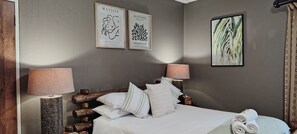 Una camera da letto con una testiera in legno, due lampade a parete, un letto con biancheria da letto bianca e due opere d'arte incorniciate sopra il letto.