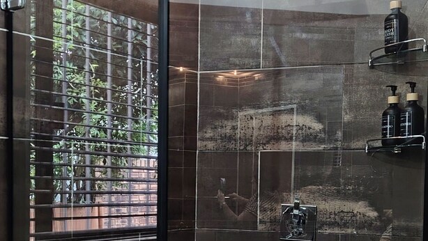 A modern bathroom with a glass shower enclosure, a bathtub, and a glass door with a view of greenery outside. - Room-indulgent Escape, Jet Bath, Stunnin (Johannesburg)