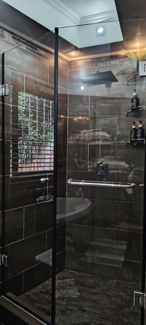 Un bagno moderno con box doccia in vetro, una vasca da bagno e una porta vetrata con vista sul verde circostante.