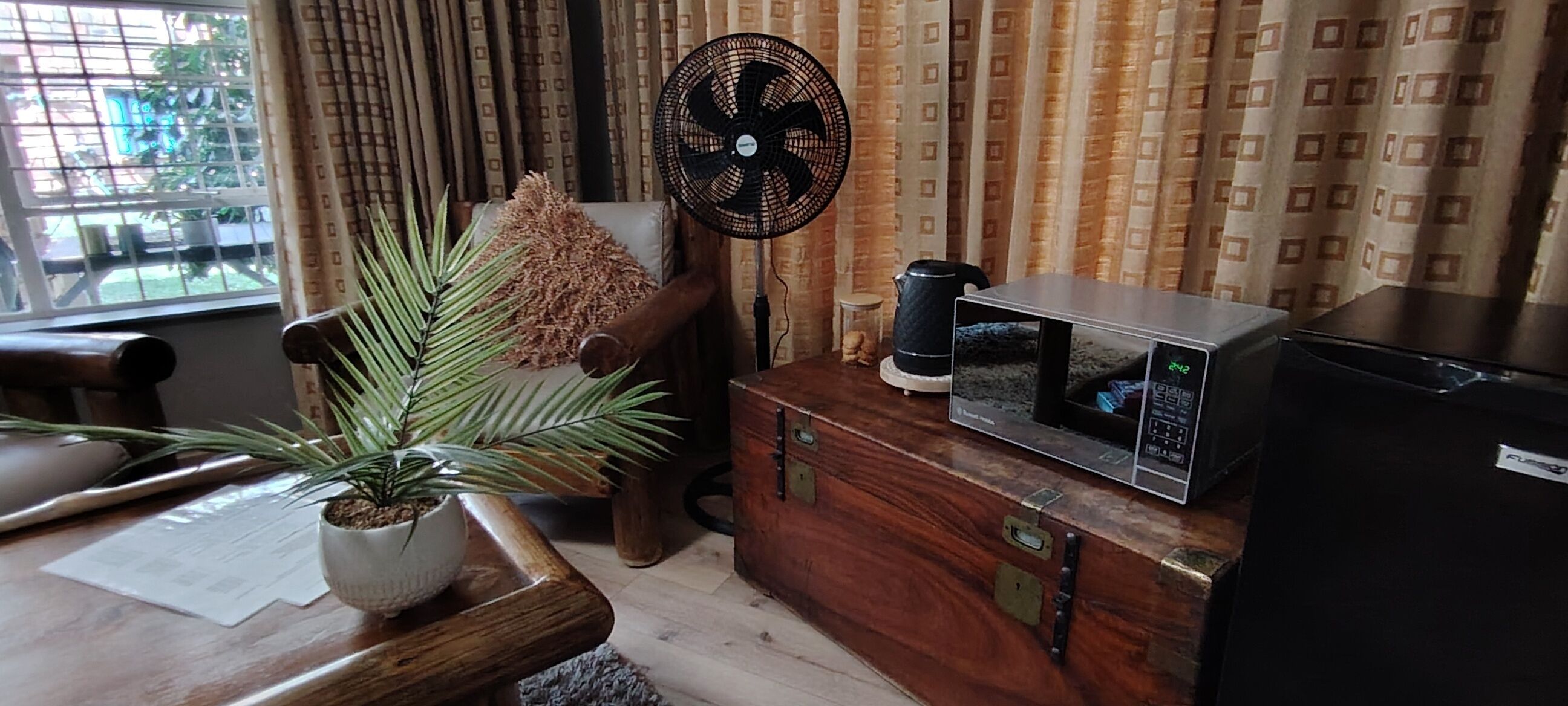 A room with a wooden cabinet, a fan, a television, and a window with curtains.