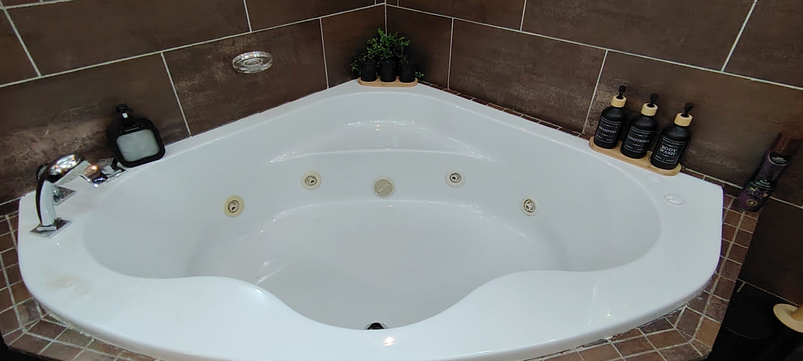 Una bañera blanca grande y separada, con múltiples jets, rodeada de azulejos marrones.