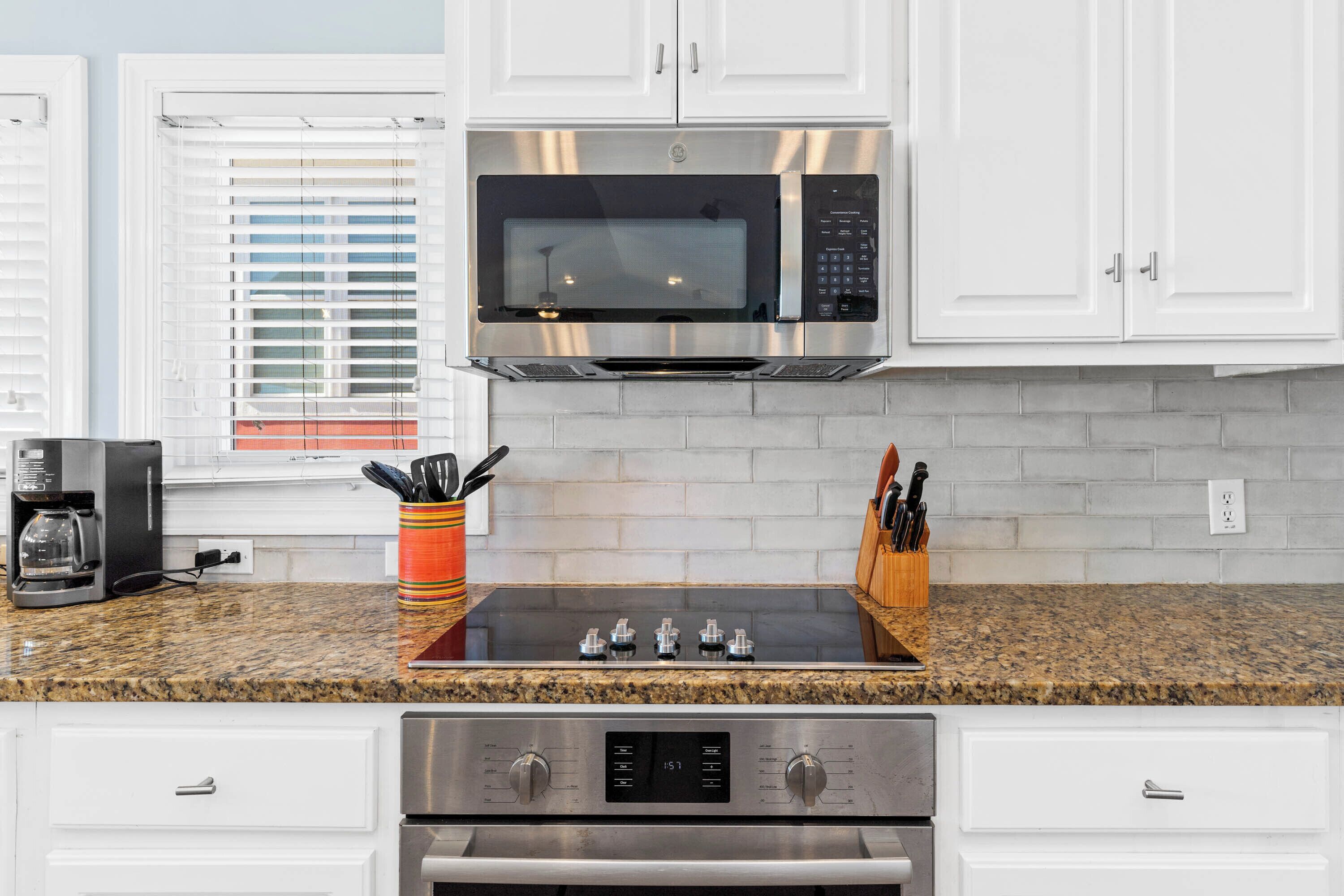 A kitchen with white cabinets, a stainless steel microwave, a gas stove, and a coffee maker.