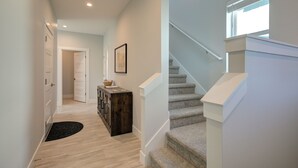 A hallway with a wooden floor, a black rug, a wooden console table, and a staircase with a white railing. - Welcome to your ultimate getaway, Burl by the Bay! (Ocean Shores)