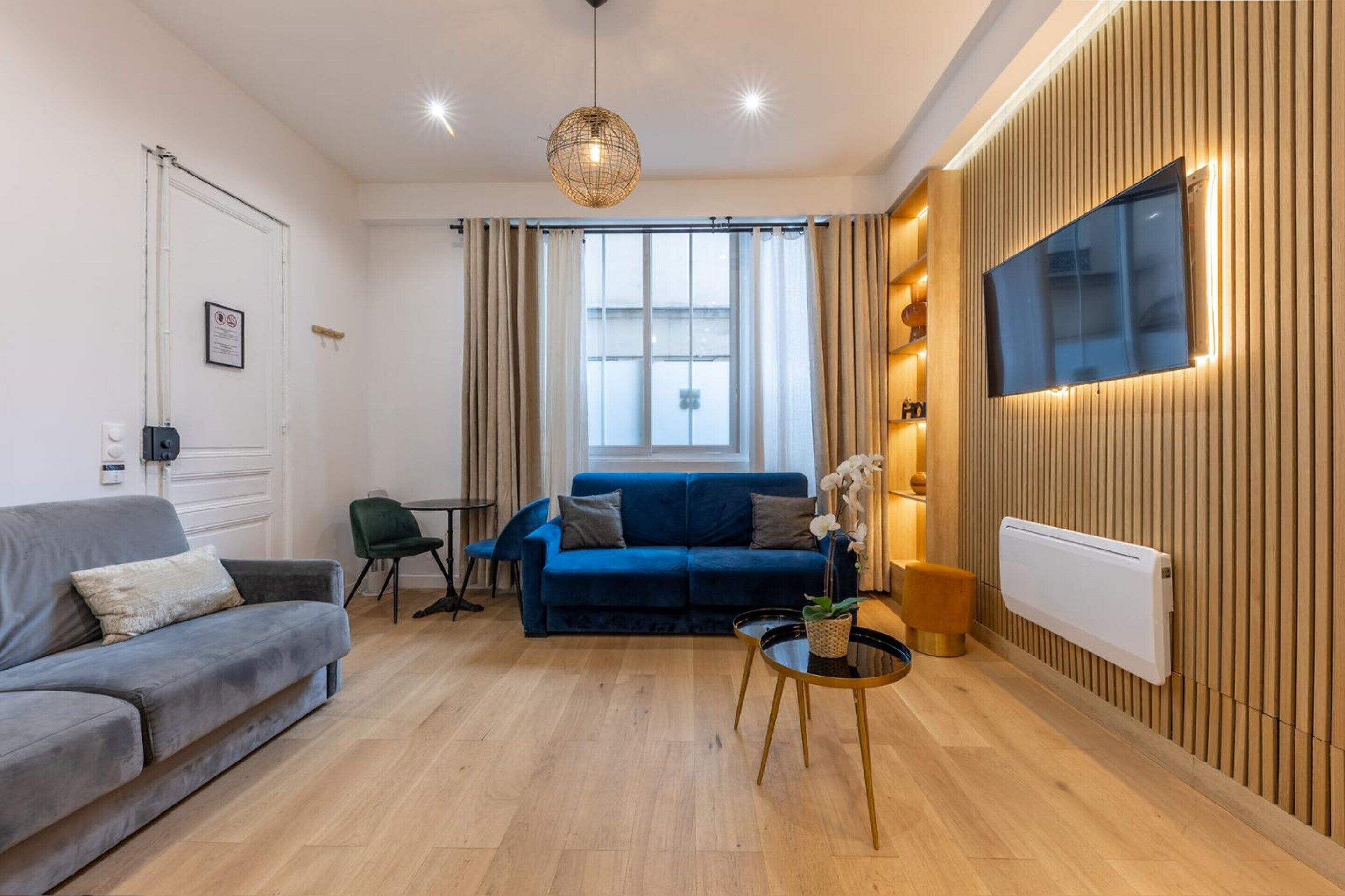 En moderne stue med en blå sofa, et rundt sofabord, en hængende lampe og et ophængt fjernsyn.