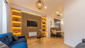 A modern living room with a blue sofa, a dining area with a table and chairs, and a kitchen in the background. - Apartment Centre de Paris Sacre Coeur (Paris)