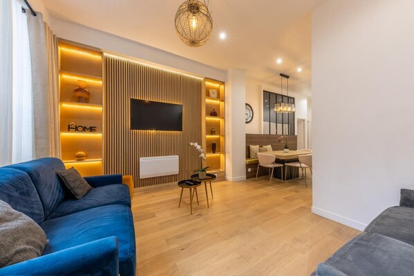 A modern living room with a blue sofa, a dining area with a table and chairs, and a kitchen in the background. - Apartment Centre de Paris Sacre Coeur (Paris)