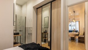 A modern hotel room with a large bed, a glass shower enclosure, a wooden wardrobe, and a dining area visible through an open door. - Apartment Centre de Paris Sacre Coeur (Paris)