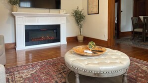 Una sala de estar con chimenea, televisor montado encima y comedor con sillas, además de un tapete decorativo.