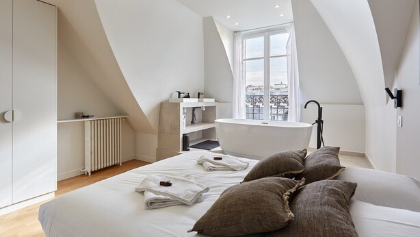 A modern bedroom with a large bed, a skylight, a built-in bathtub, and a view of the city. - Superb Apartment Arc de Triomphe/ Trocadero (Paris)