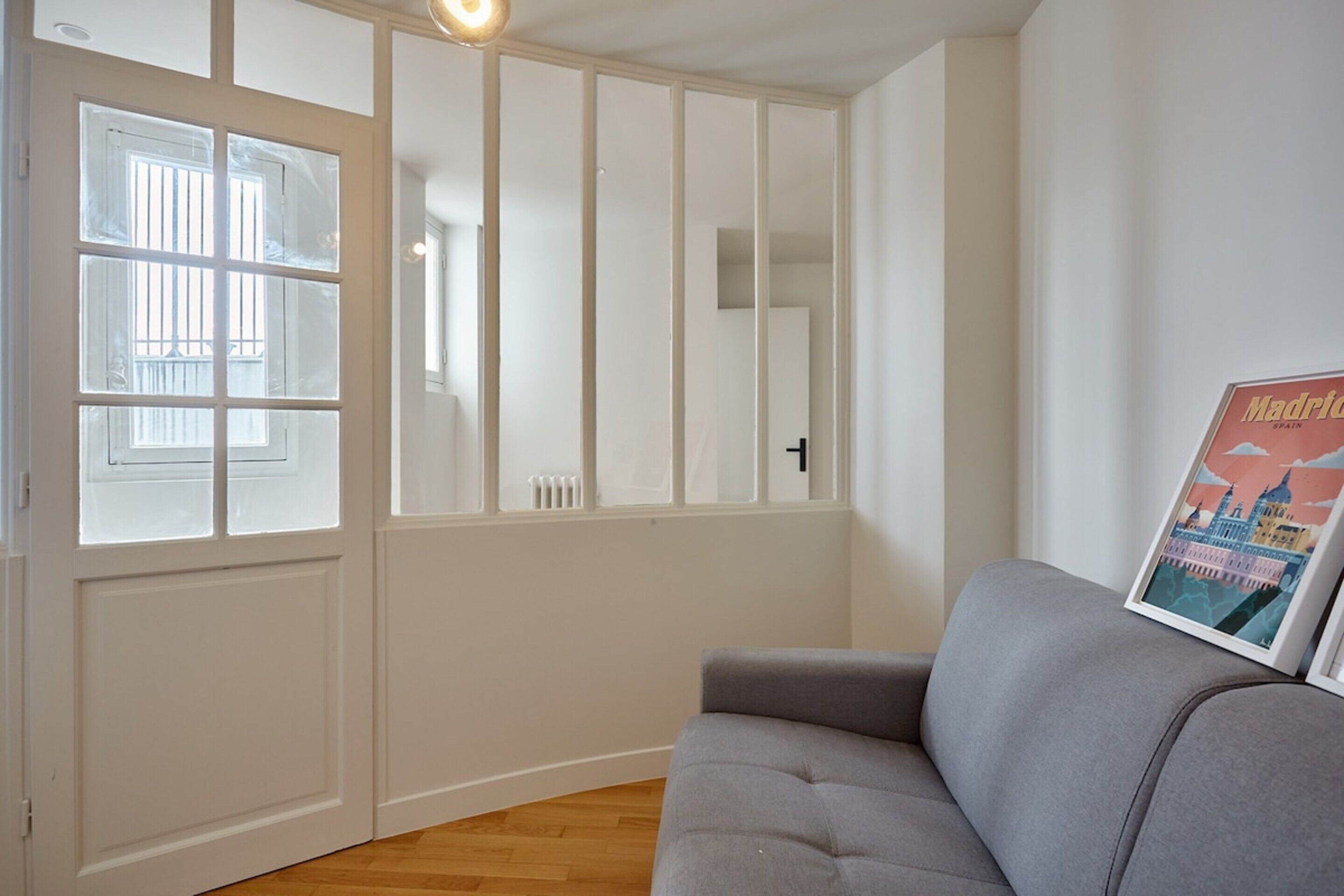 A room with a grey sofa, a white wardrobe, and a window with blinds.