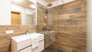 Ein modernes Badezimmer mit einer Wandgestaltung aus Holz, einer Duschkabine aus Glas und einem weißen Waschbecken.
