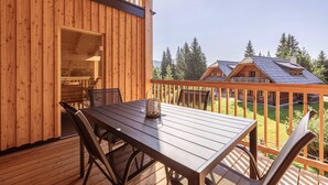 A wooden deck with a table and chairs, overlooking a forested area with cabins. - Ferienwohnung mit 2 Schlafzimmern & Sauna (Oberwölz)