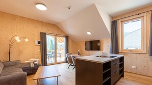 A modern interior with a wooden floor, a sofa, a dining table, a kitchen island, and a TV mounted on the wall. - Ferienwohnung mit 2 Schlafzimmern & Sauna (Oberwölz)