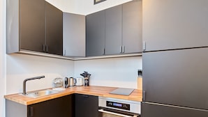 A compact kitchen with dark cabinets, a wooden countertop, a built-in oven, and a dishwasher. - Suite Saint Germain des Pres Rue de Rennes (Paris)