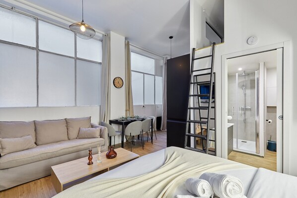 A modern hotel room with a sofa, a bed, a dining table, and a shower area. - Apartment Suite Saint Germain / Rue de Rennes (Paris)