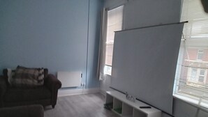 A room with a whiteboard, a brown sofa, and a window with blinds. - Sunny Seaside Apartment in Blackpool (Blackpool)