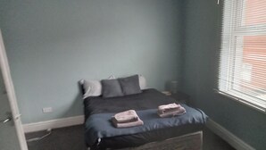 A bedroom with a bed, pillows, and a window with blinds. - Sunny Seaside Apartment in Blackpool (Blackpool)