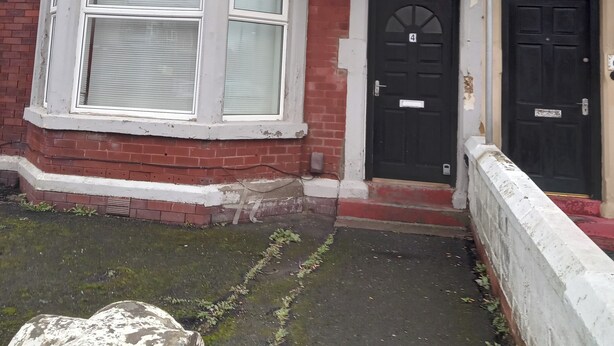 A two-story brick house with a black front door, white-framed windows, and a small front yard with a stone feature. - Sunny Seaside Apartment in Blackpool (Blackpool)