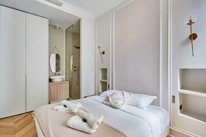 A hotel room with a bed, a bathroom with a shower, a vanity with a mirror, and a rose decoration on the wall. - Magnificent Apartment Etoile (Paris)
