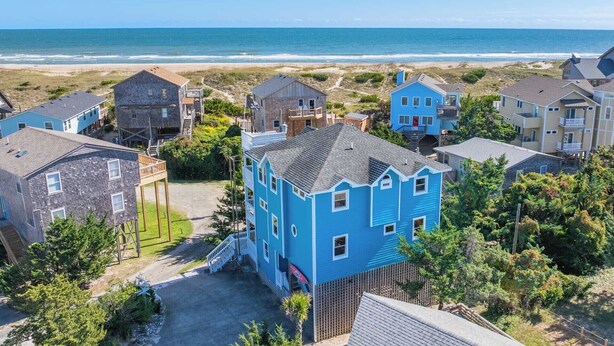 Ein Küstenwohngebiet mit Häusern, darunter ein markantes blaues Haus mit einer Veranda und Blick auf den Strand.