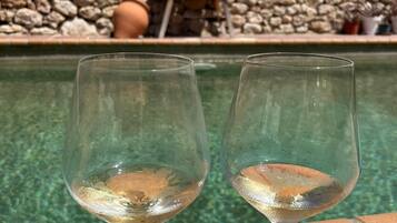 Two empty wine glasses on a brick ledge by a pool with a stone wall in the background.