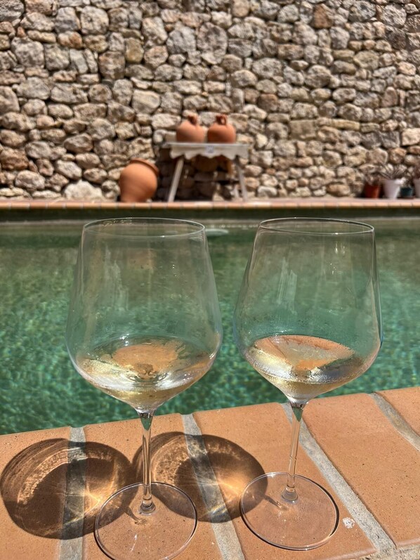 Deux verres à vin vides sont posés sur une étagère en briques, près d’une piscine, avec un mur de pierre en arrière-plan.