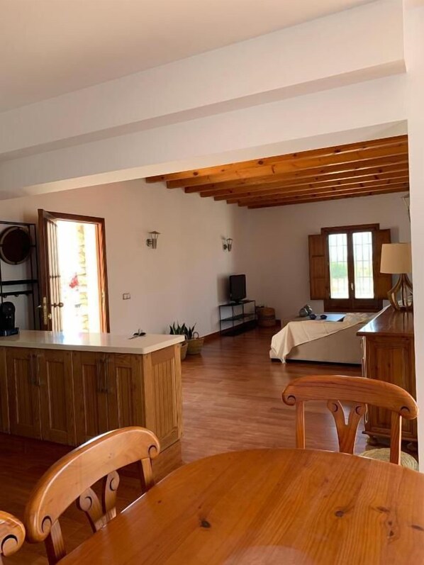 Une pièce spacieuse comprenant une table à manger en bois, des chaises, un coin cuisine et un téléviseur.