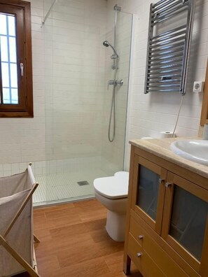 Une salle de bain avec une douche à parois de verre, des toilettes blanches et un meuble-lavabo en bois avec un évier.