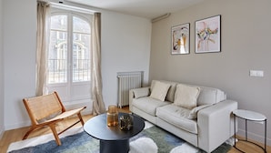Een woonkamer met een bank, een stoel, een bijzettafeltje en kunstwerken aan de muur.