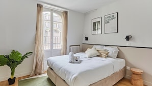 Een moderne slaapkamer met een groot bed, een potplant en uitzicht op een gebouw door een raam.
