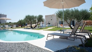 A swimming pool with lounge chairs and an umbrella, surrounded by olive trees and modern buildings. - Tower House in Puglia With Pool and Charm (Cisternino)