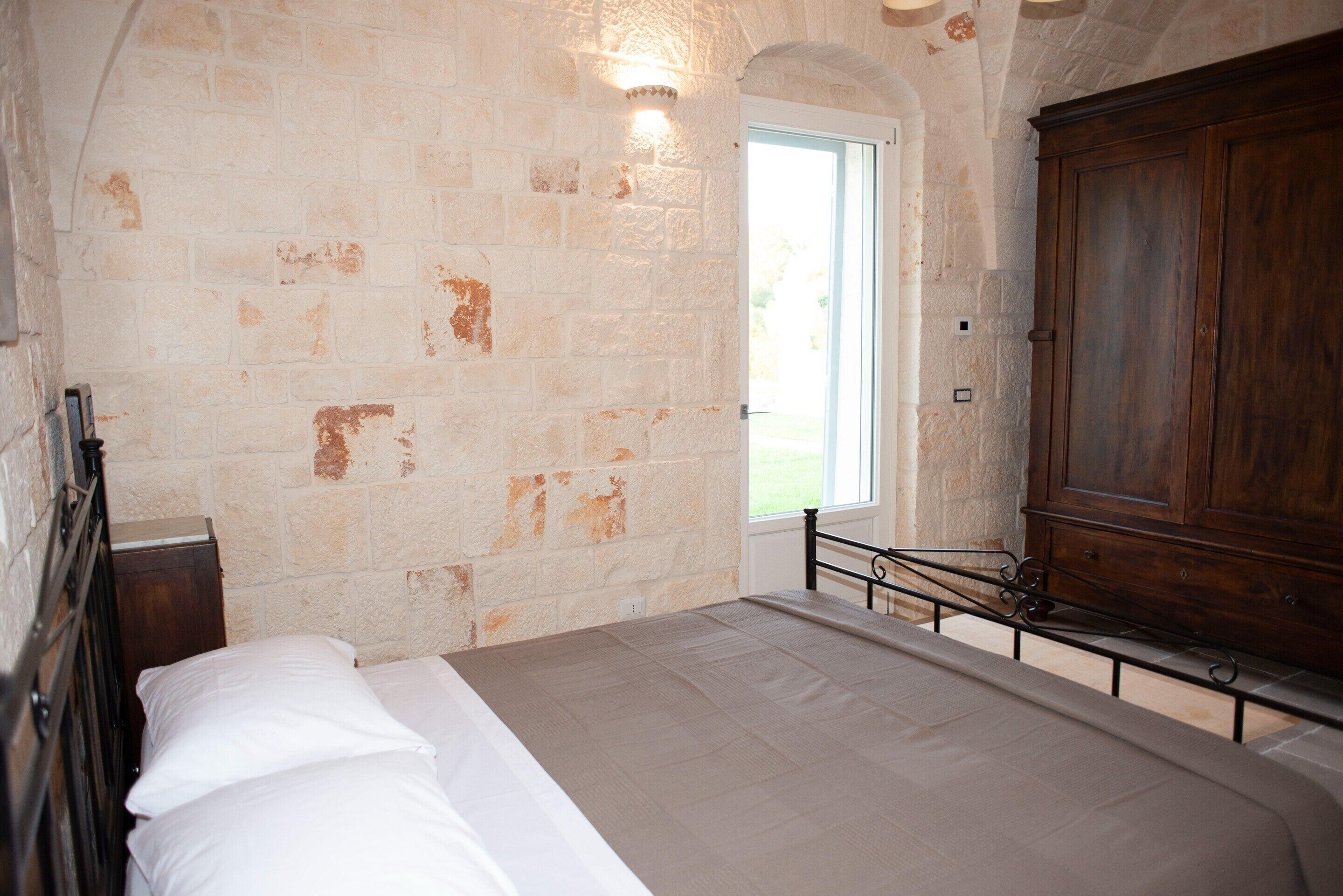 A bedroom with a bed, a wooden wardrobe, and a stone wall.