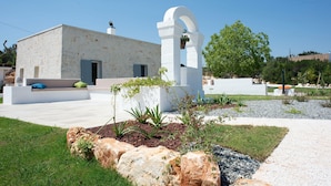 A modern building with a white facade, a stone bench, and a garden area with plants and rocks. - Tower House in Puglia With Pool and Charm (Cisternino)