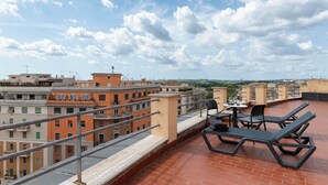 Terraza en la azotea con mesa y sillas, con vista a un paisaje urbano de edificios y cielo despejado.