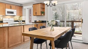 A modern kitchen with wooden cabinets, a white microwave, and a dining area with a wooden table and chairs. - Woodbridge 07A (Snowmass Village)
