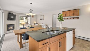A modern kitchen with a central island, built-in oven, and a dining area with a fireplace. - Woodbridge 07A (Snowmass Village)