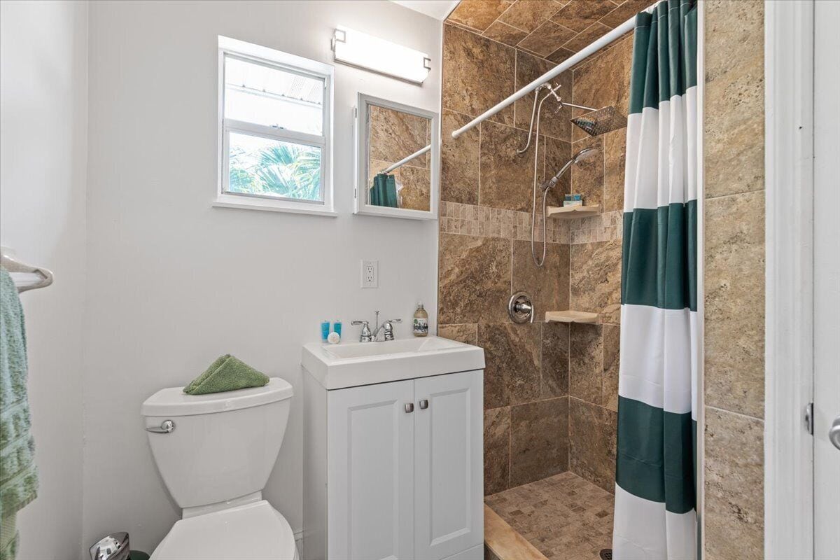 A bathroom with a toilet, sink, mirror, shower, and a towel rack.