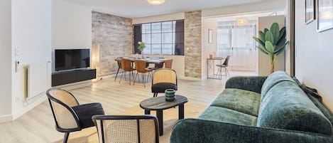 A modern living room with a green sofa, a TV, and a dining area with a table and chairs.
