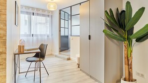 Ein modernes Interieur mit Holzboden, Schreibtisch und Stuhl, einer großen Kühlpflanze und einer Schiebetür zu einem weiteren Raum.