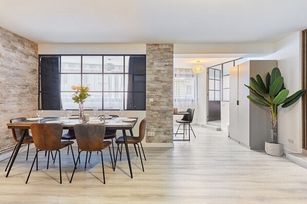 A modern dining area with a wooden table and chairs, a potted plant, and a view through large windows. - New Apartment Saint Germain Invalides (Paris)