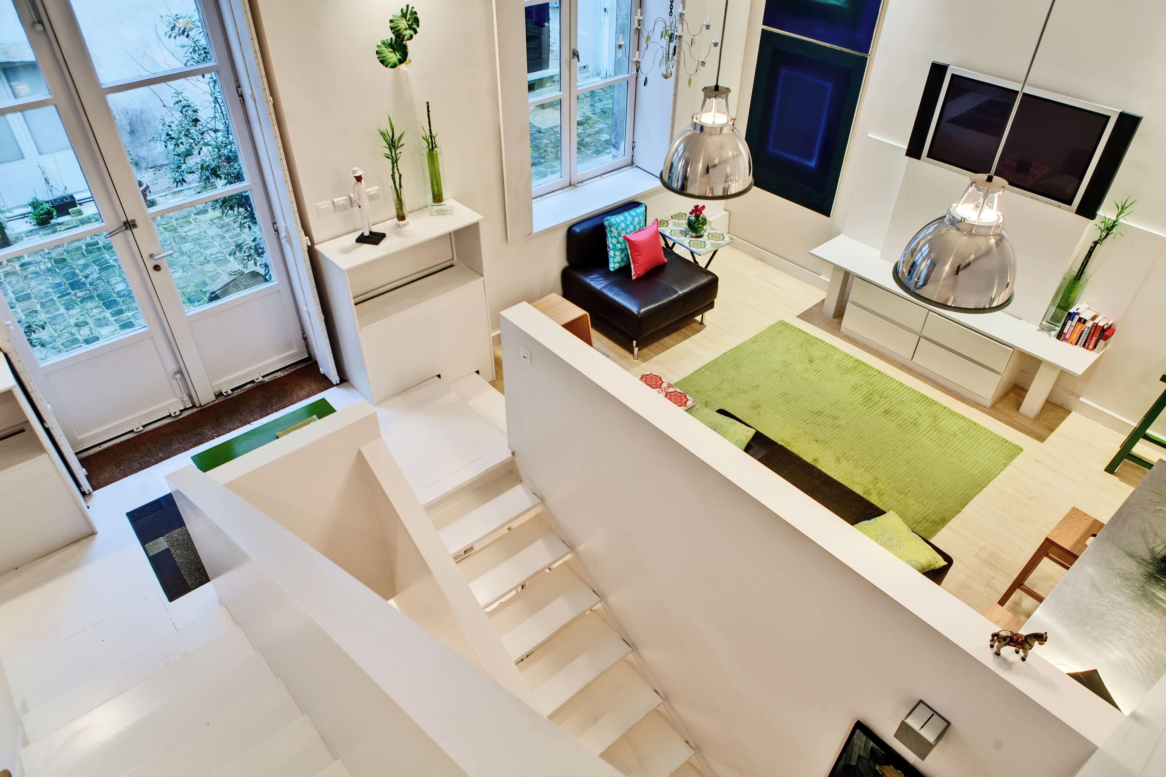 A modern living space with a staircase, a sofa, a dining area, and a large window offering a view of the outdoors.