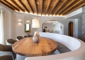 Un intérieur moderne avec un plafond en bois, une table ronde en bois agrémentée d’un vase et un banc blanc aux lignes courbes.