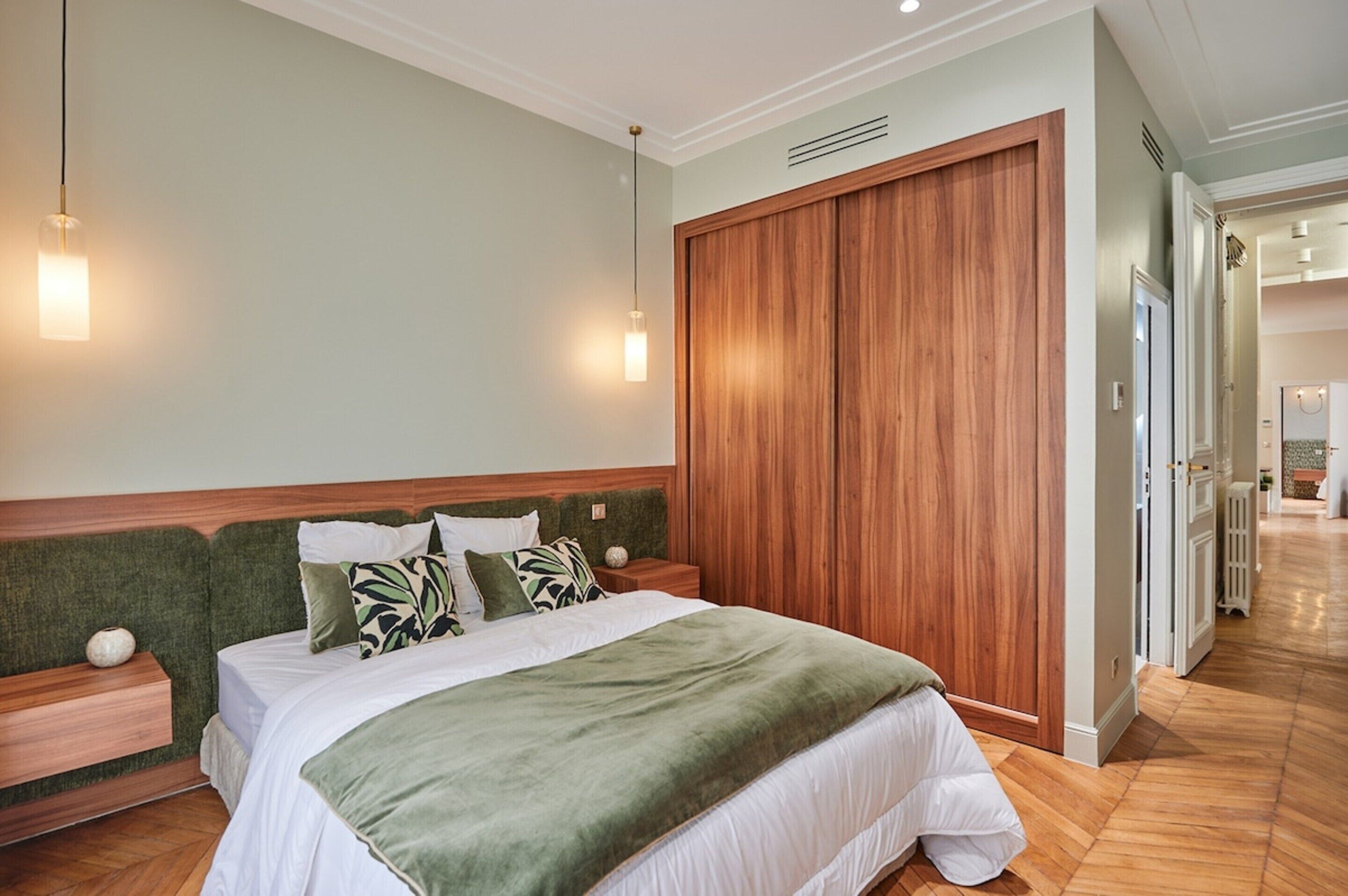 A neatly arranged bedroom with a large bed, wooden headboard, two bedside tables, and a wardrobe.